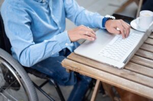 a man in a blue shirt sitting in a wheelchair and using a laptop