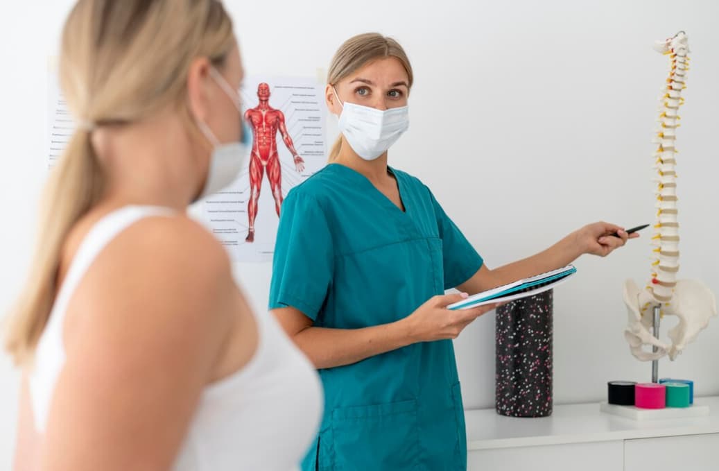 Healthcare professional pointing at a spine model, explaining to a patient