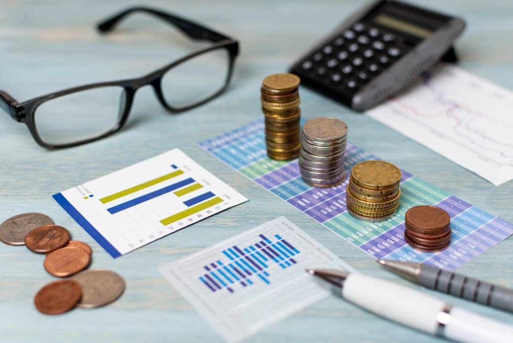 Financial charts with glasses, coins, and a calculator on a blue surface