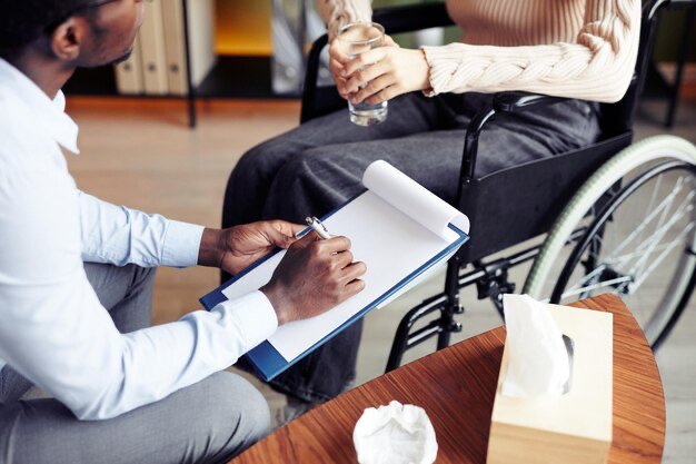 A man listens to a woman in a wheelchair and writes something in a notebook