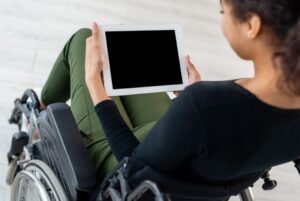 Over-the-shoulder view of a woman in a wheelchair holding a tablet with a blank screen