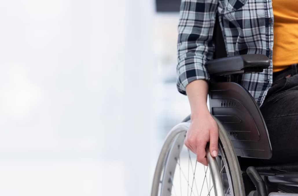 Person in a wheelchair with a hand on the wheel, wearing a plaid shirt