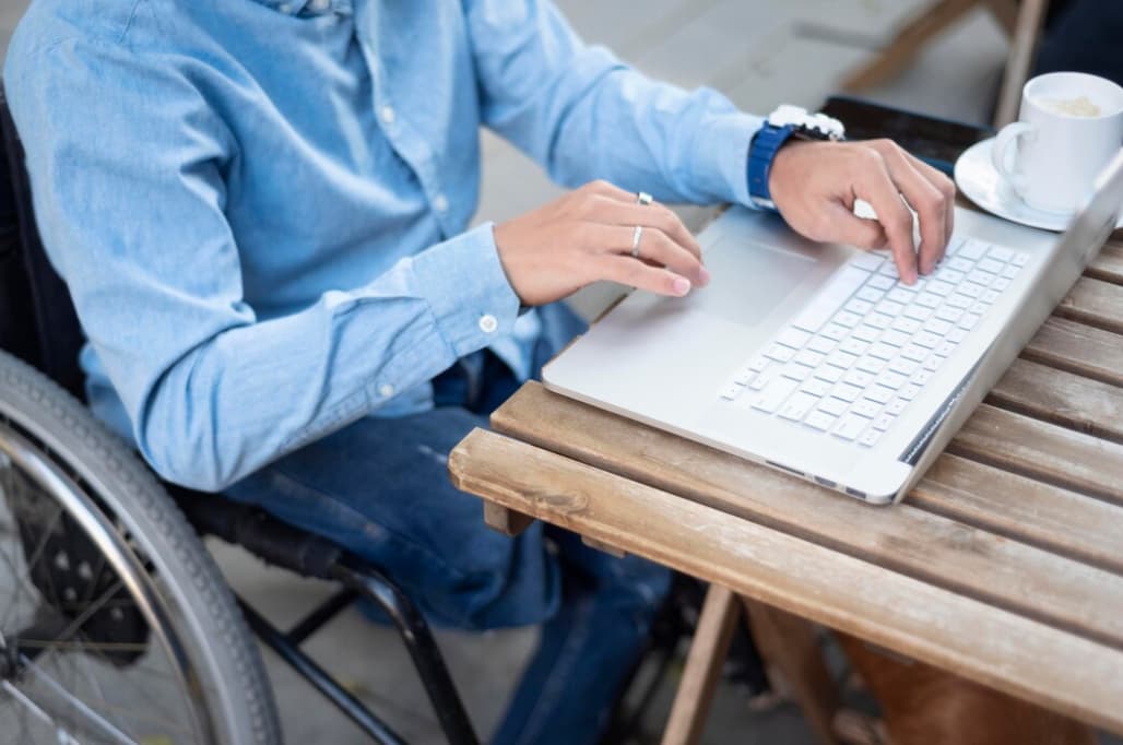 Close-up of a person in a wheelchair using a laptop on a wooden table