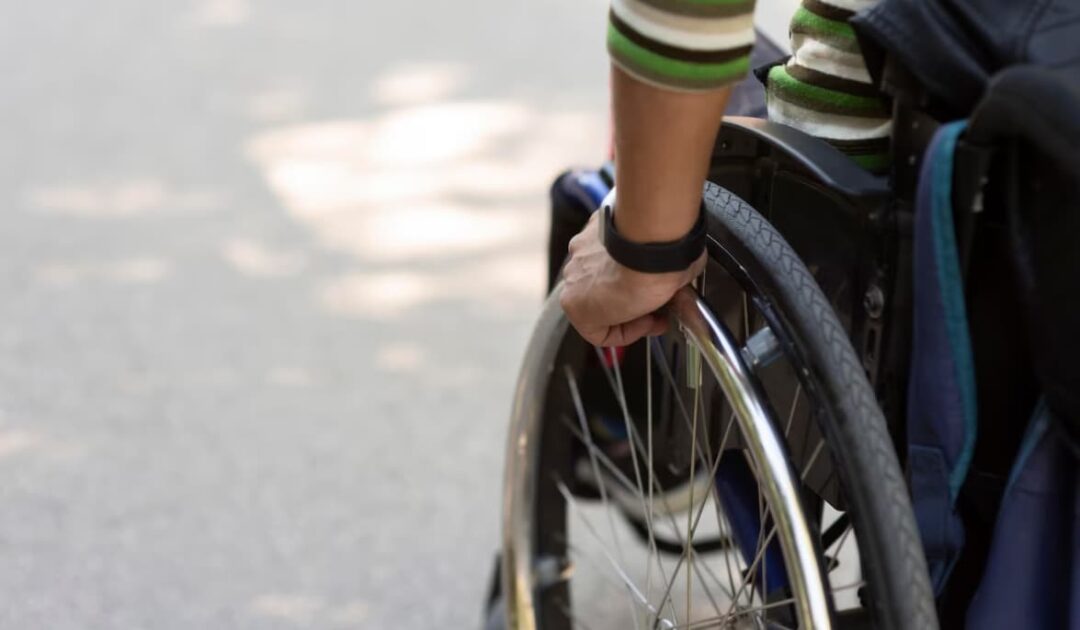 a hand on a wheelchair's wheel, outdoors with natural light