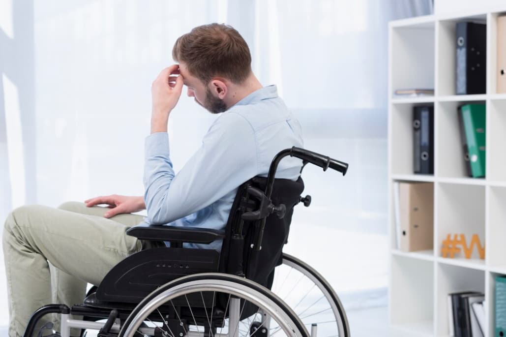 Distressed man in wheelchair by desk with head in hand